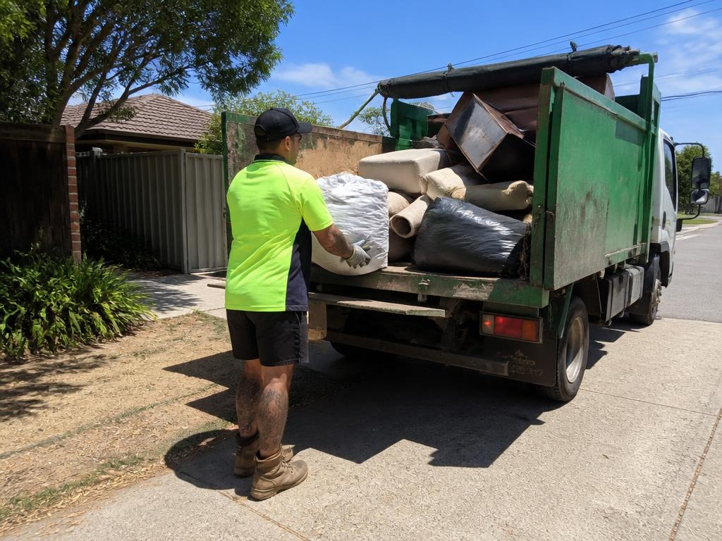 Friendly rubbish removal worker loading a green bin into a truck on a suburban street